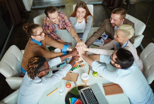 Several managers making pile of hands over workplace